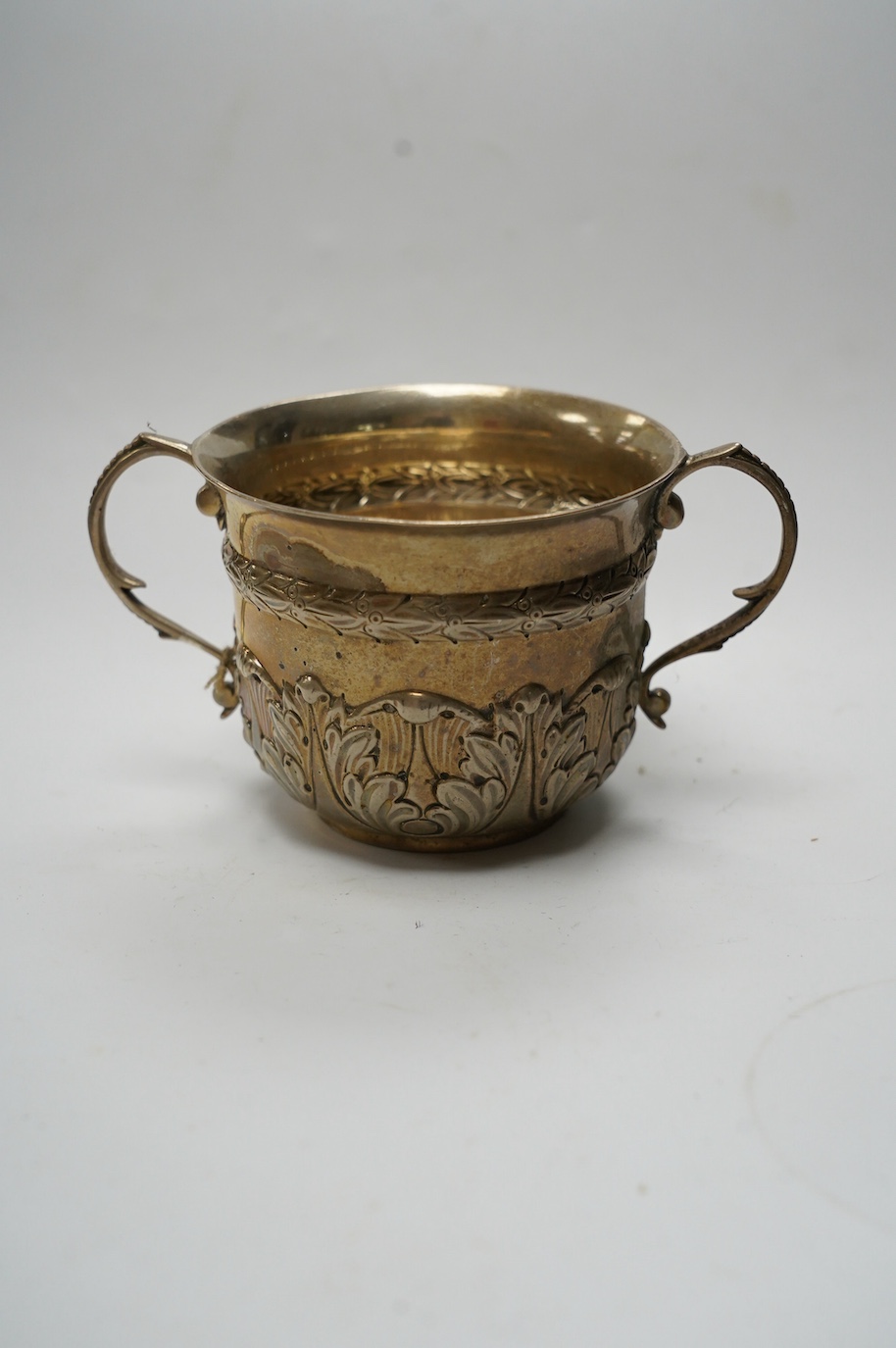 An Edwardian repousse silver porringer, Daniel & John Welby, London, 1905, height 73mm, together with a late Victorian silver two handled sugar vase with blue glass liner, London, 1895. Condition - fair